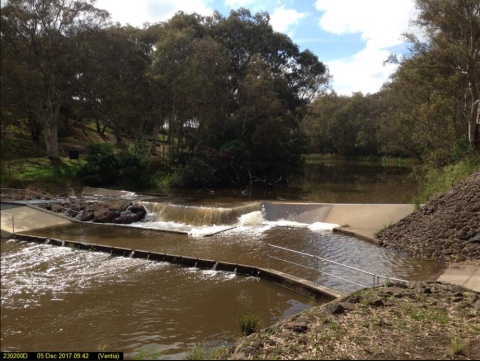 This image shows is looking upstream at an artificial crump weir. Water is flowing over the structure.